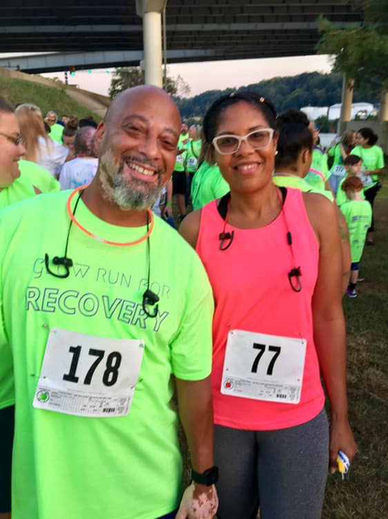 two running participants smiling in front of crowd of vibrant shirts